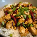 Freshly cooked chicken stir fry with vegetables over rice, topped with colorful chili peppers and crushed peanuts for added flavor and crunch. Perfect for quick, flavorful meals.